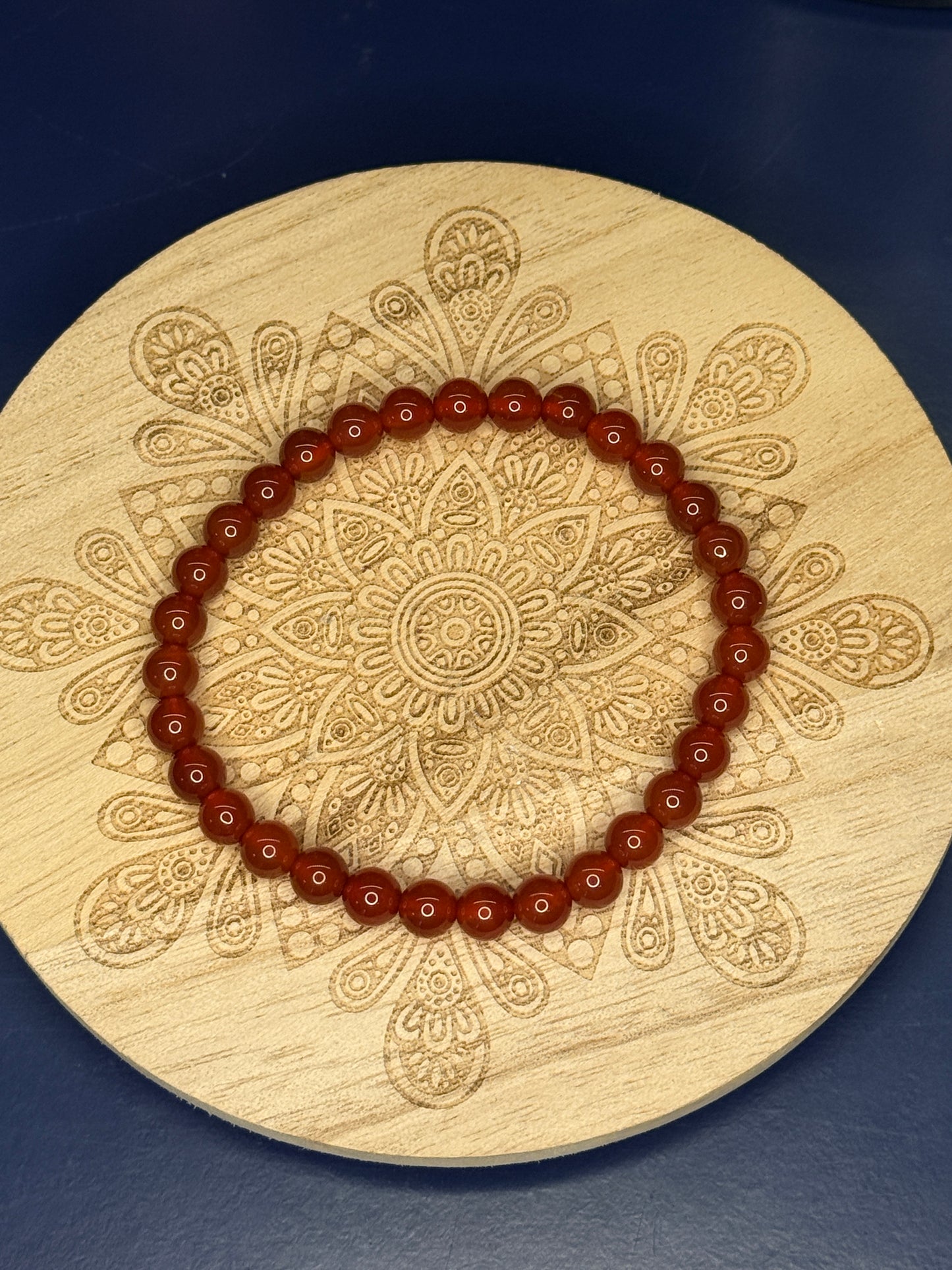 Red beaded zebra jasper bracelet resting on a decorative wooden coaster on a blue background