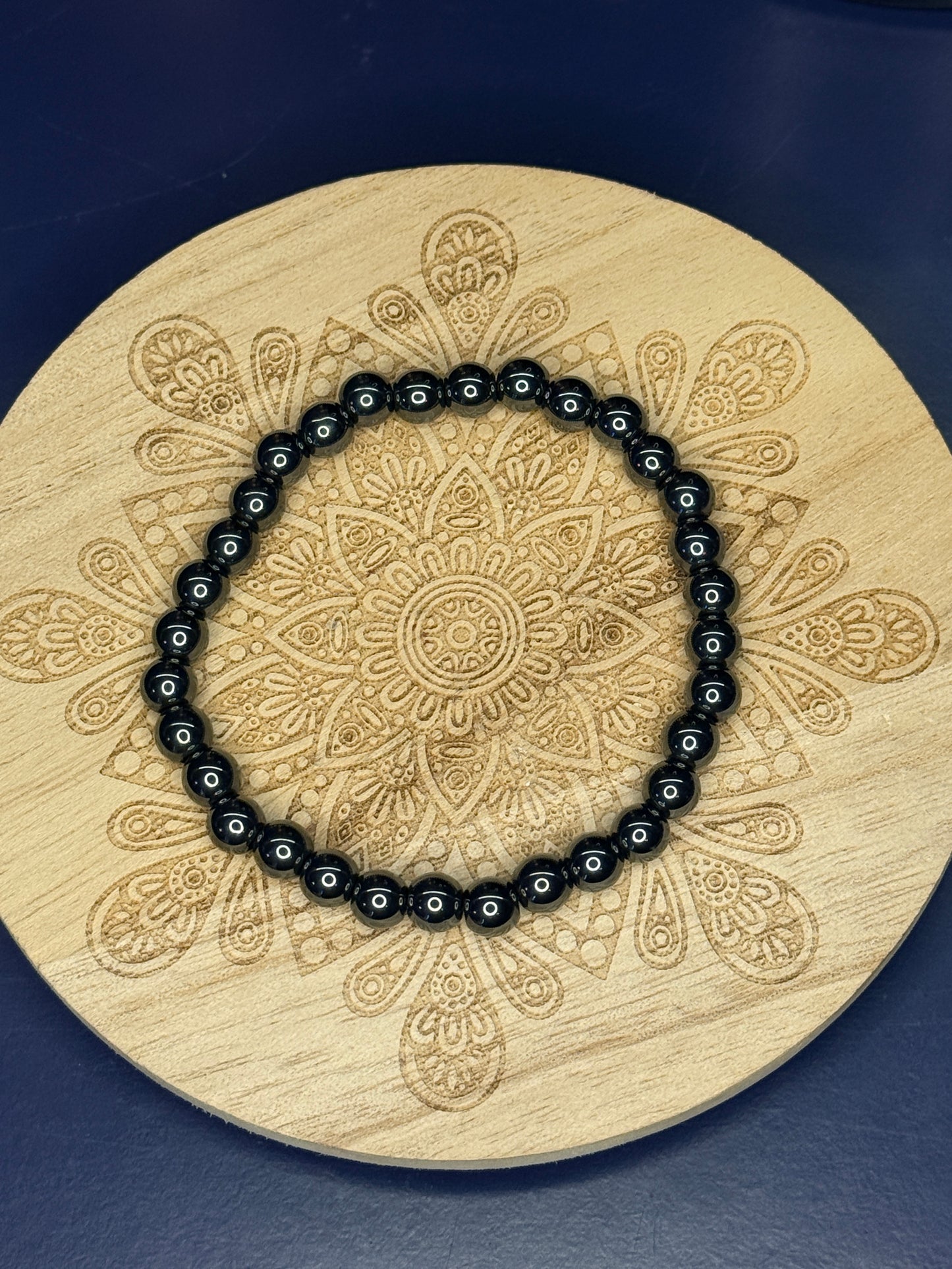 Black shining beaded hematite bracelet resting on a decorative wooden coaster on a blue background