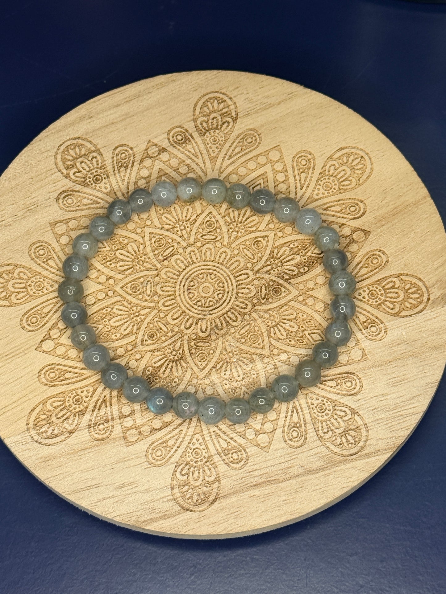 Grey beaded labradorite bracelet resting on a decorative wooden coaster on a blue background