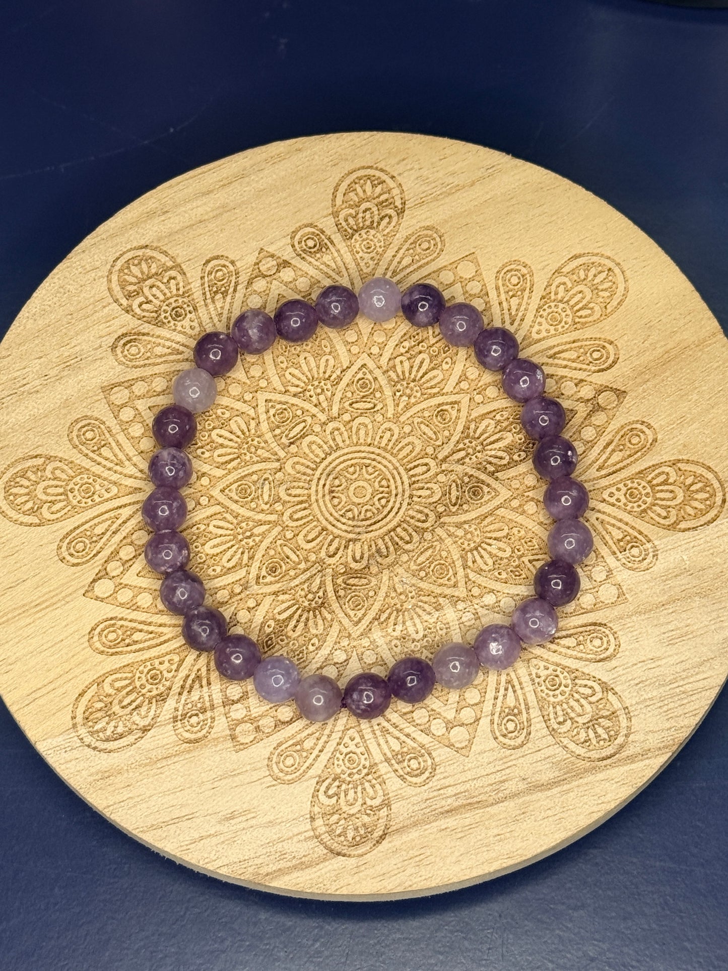 Purple beaded lepidolite bracelet resting on a decorative wooden coaster on a blue background