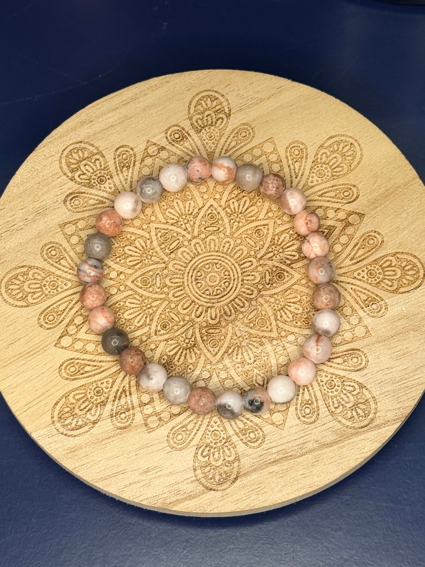 Beaded pink zebra jasper bracelet resting on a decorative wooden coaster on a blue background