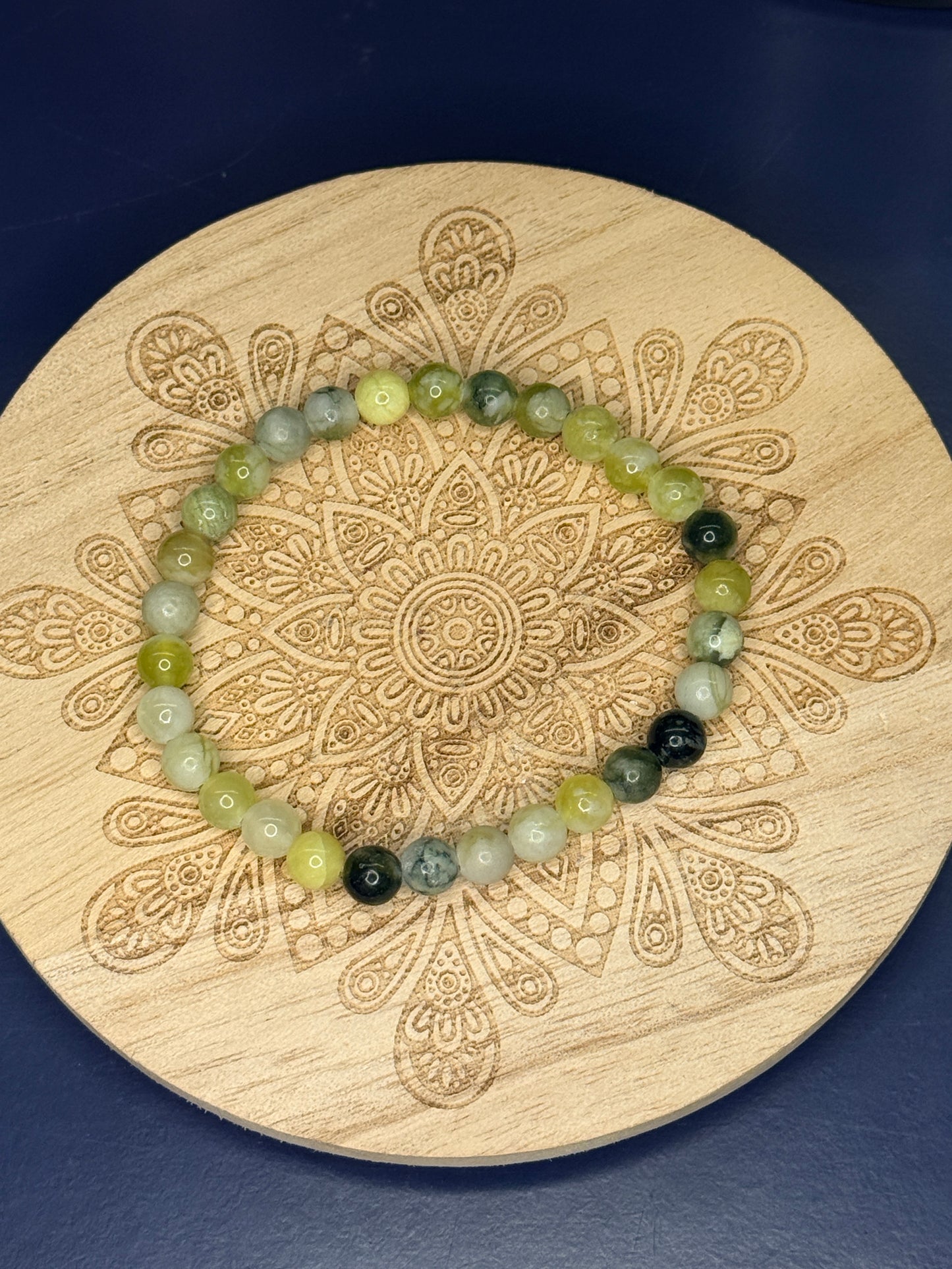 Green and yellow beaded serpentine bracelet resting on a decorative wooden coaster on a blue background