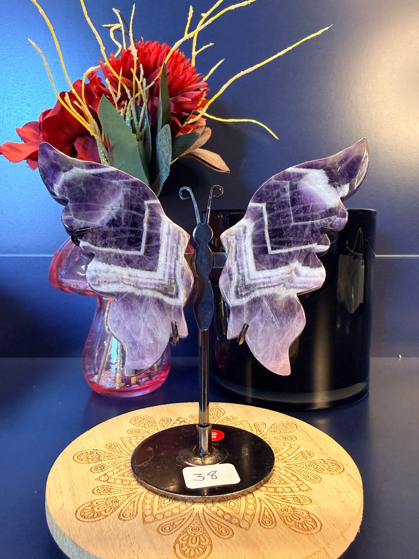 Large purple crystal butterfly wings sitting on a decorative wooden coaster in front of a glass mushroom and black jar