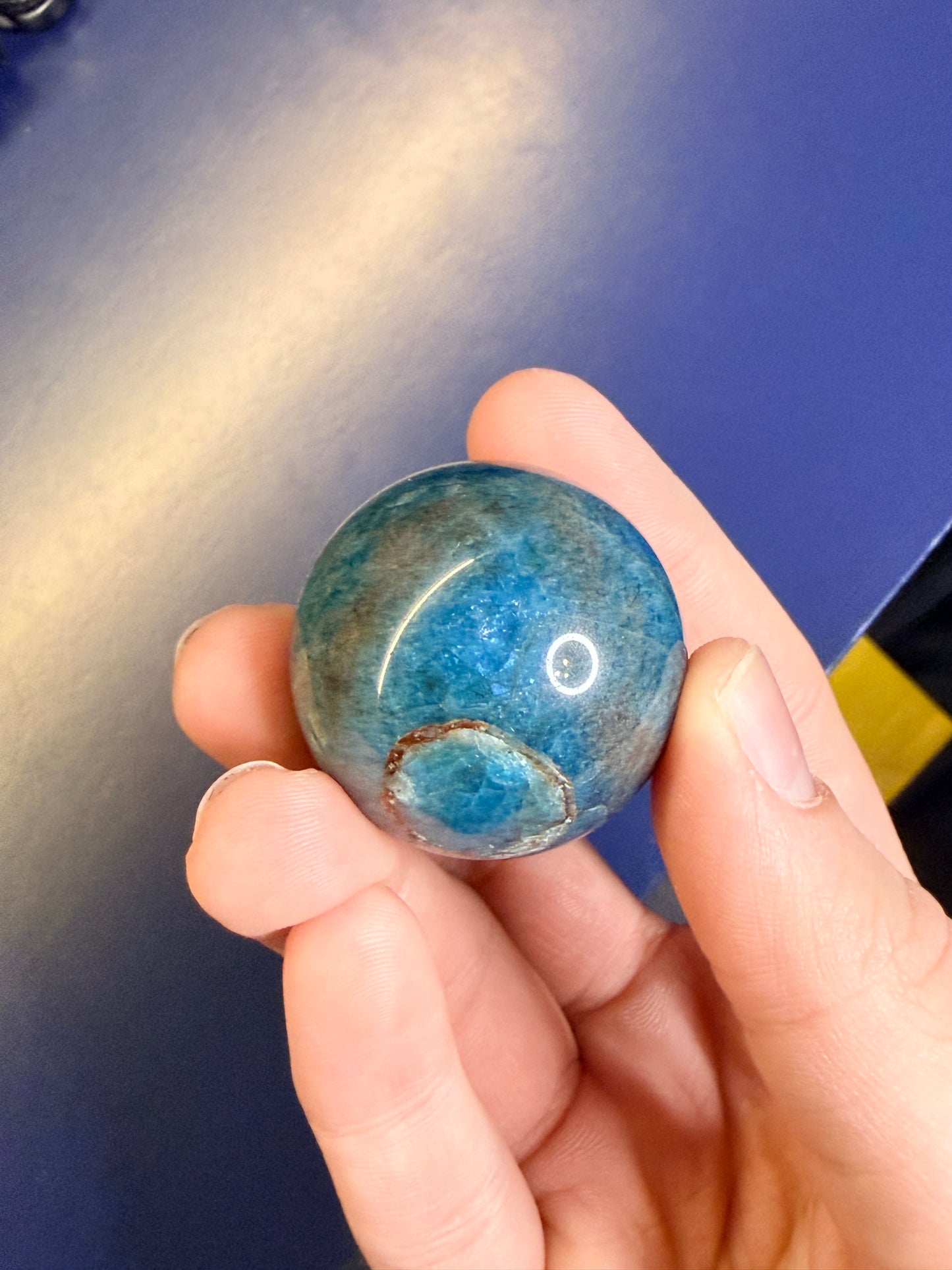 A hand holding a blue apatite sphere against a blue background