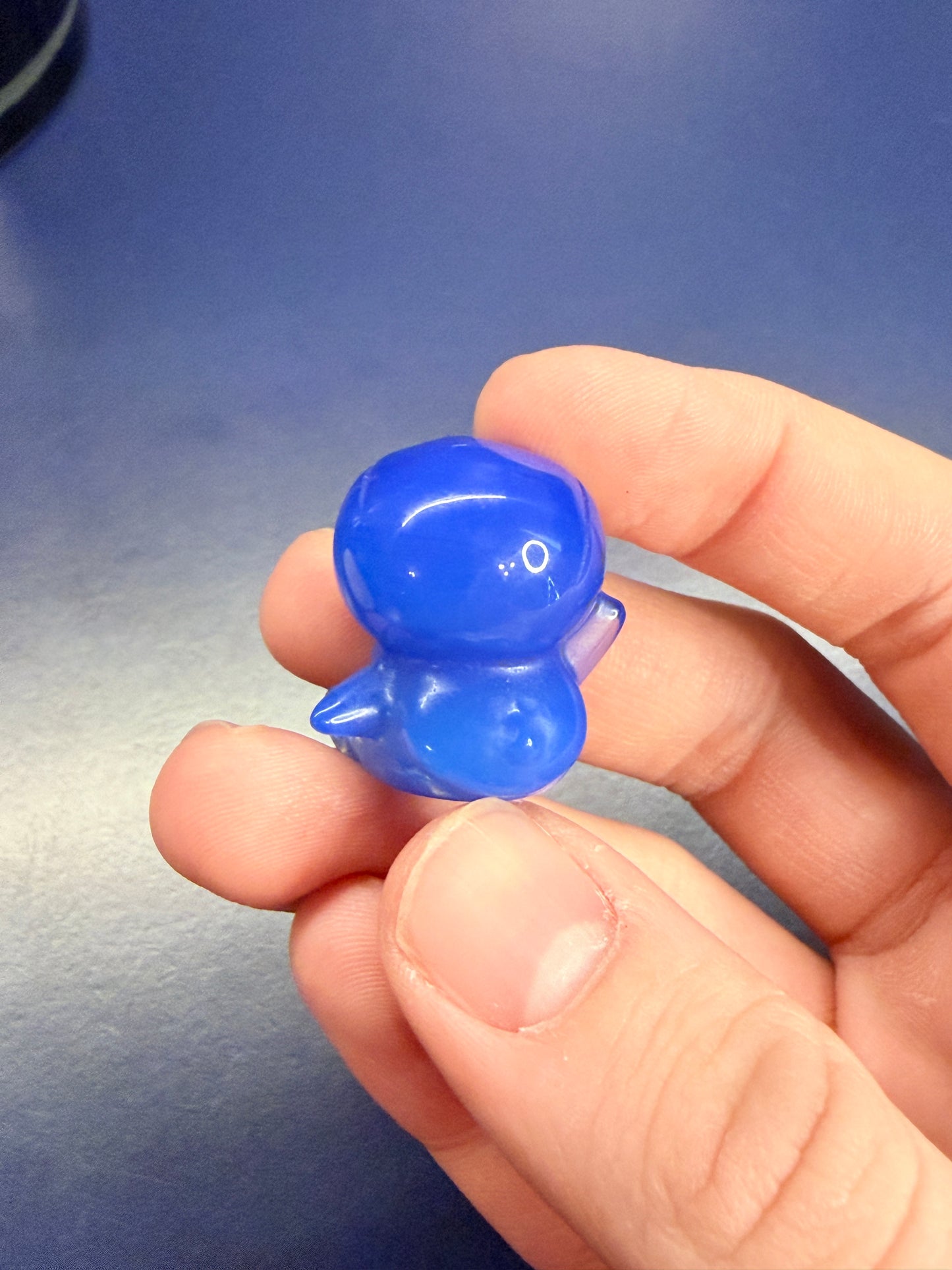 Hand holding a blue opalite piplup crystal against a blue background