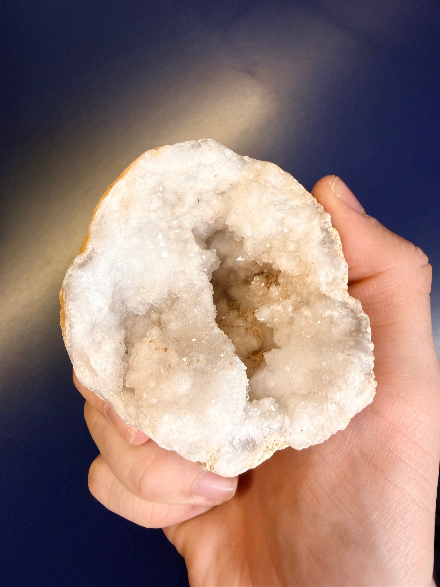 Hand holding a crystal geode against a blue background