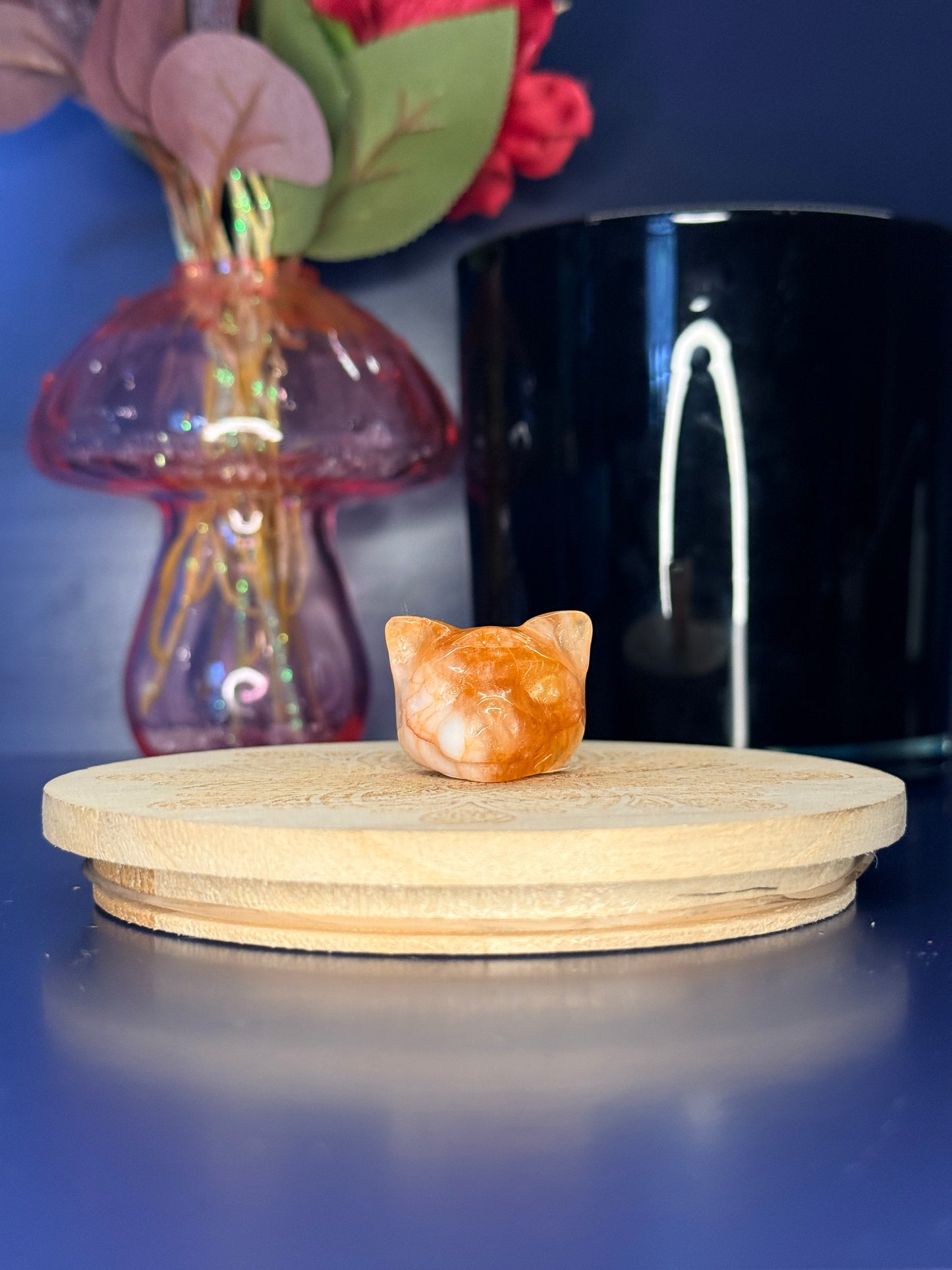 White and orange wolf head quartz carving in front of a pink vase and black jar on a wooden coaster against a blue background
