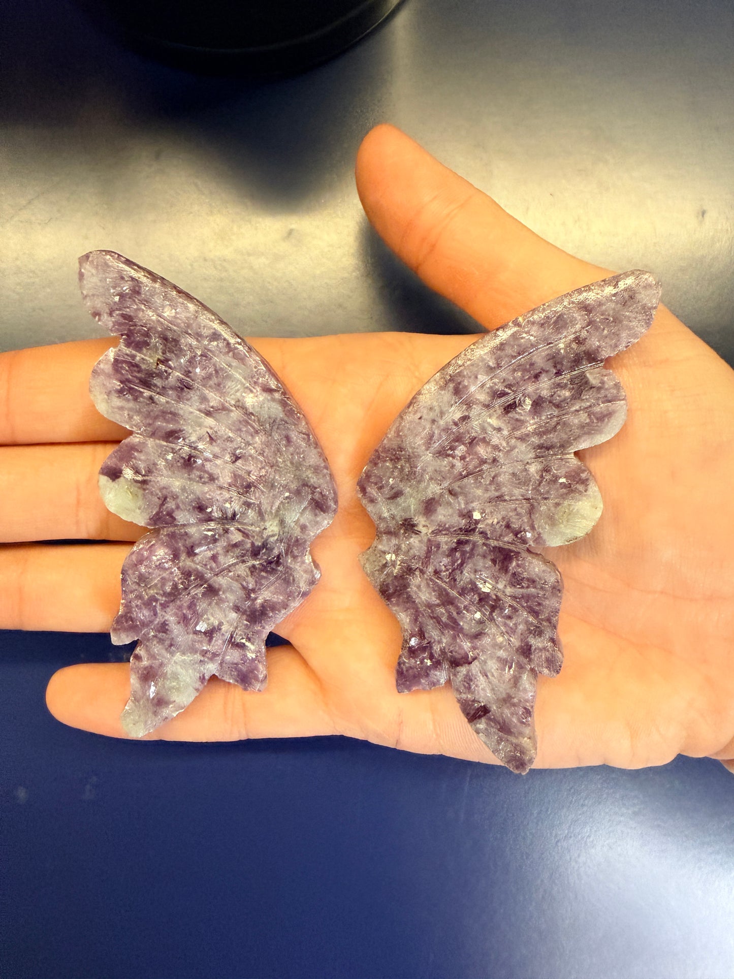 Hand holding two large purple lepidolite butterfly wings against a blue background