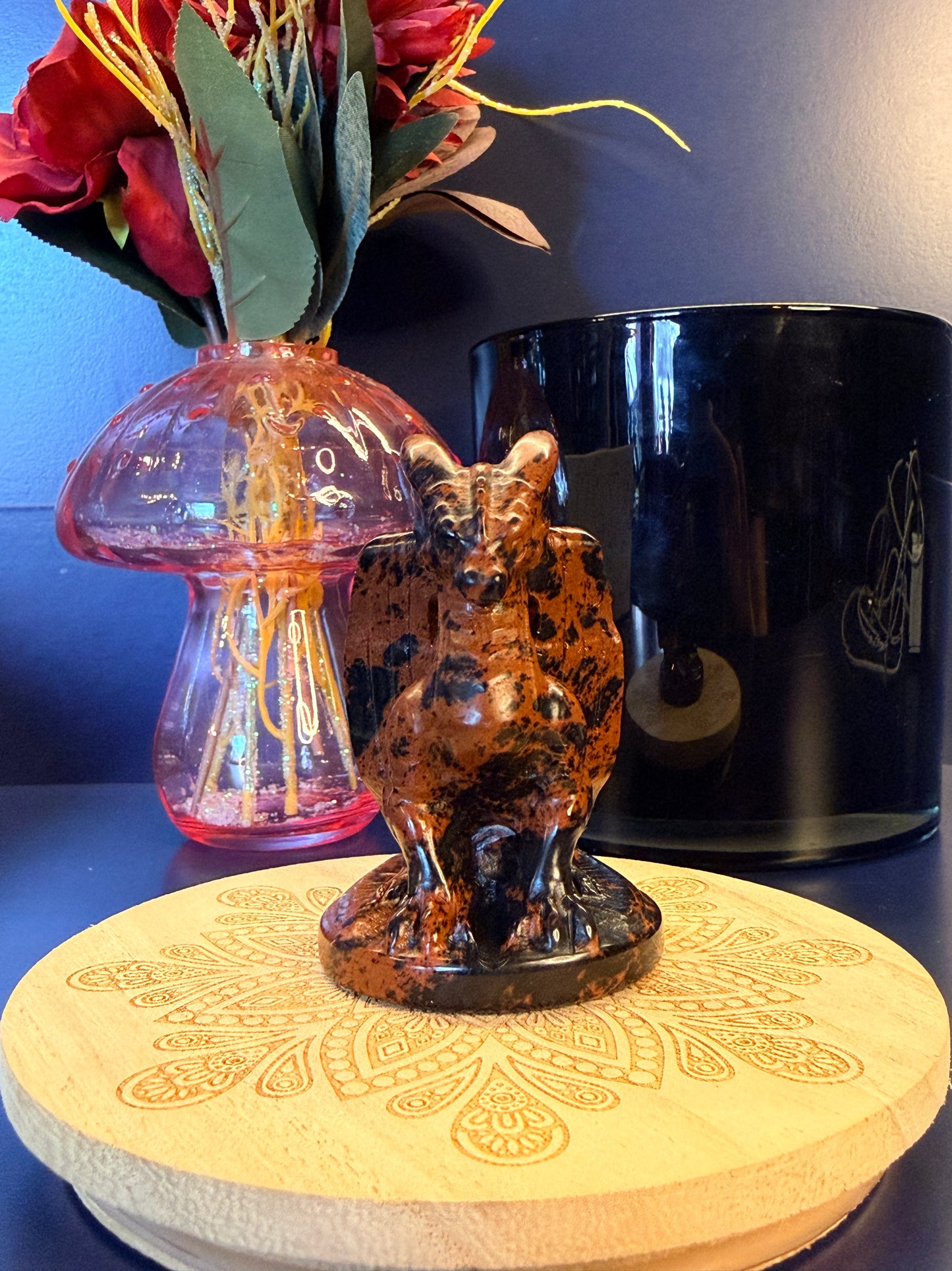A large mahogany obsidian dragon sitting on a decorative wooden coaster in front of a glass mushroom and black jar