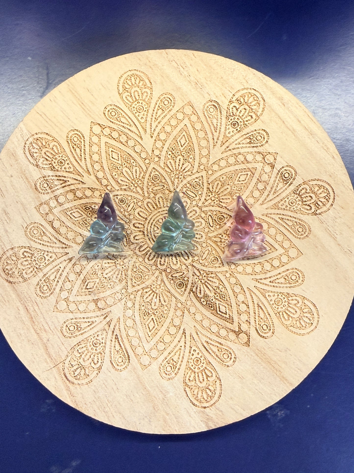 Three faerie shaped fluorite crystals sitting on a decorative wooden coaster on a blue background