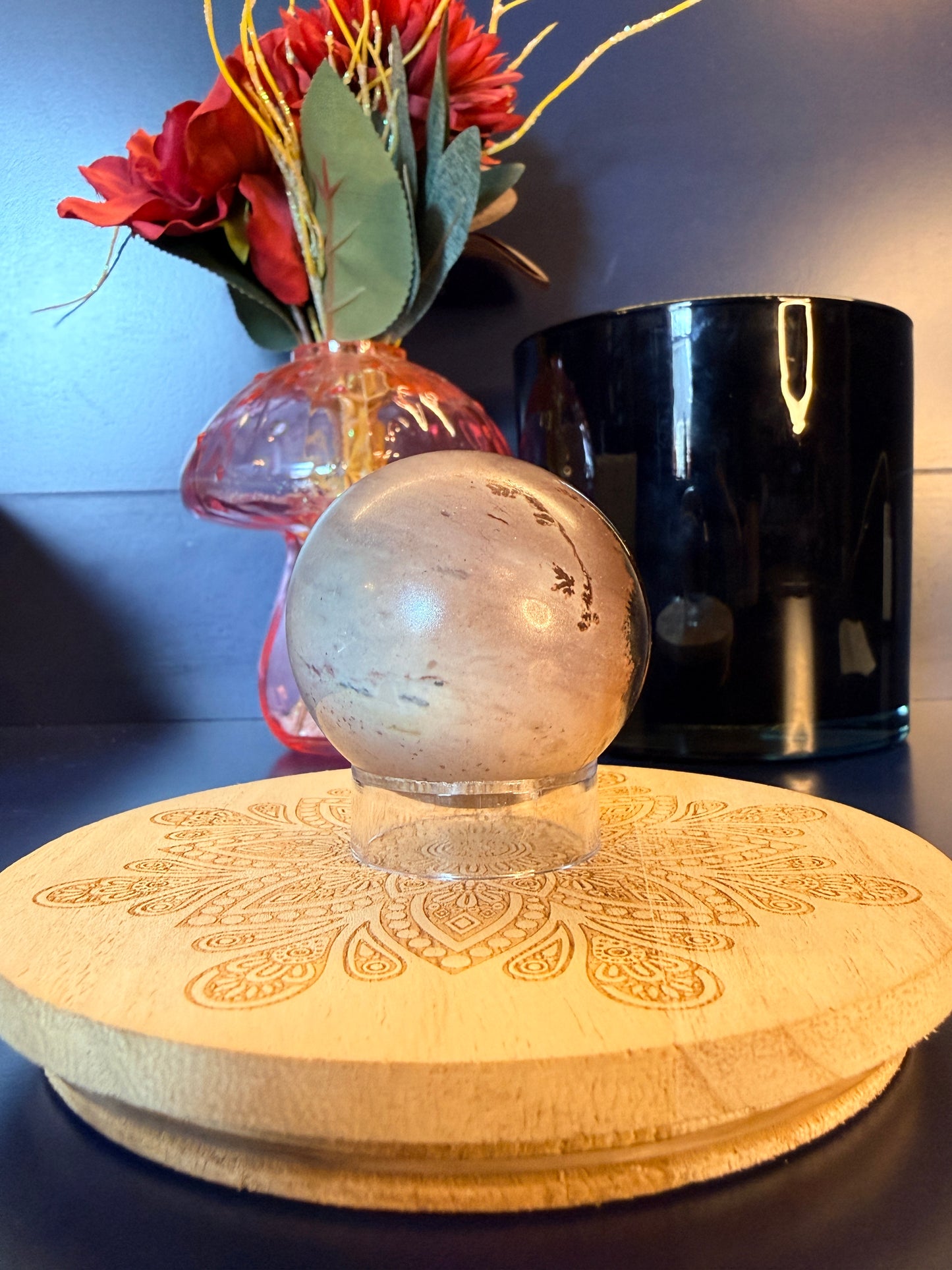 Light grey and purple picture Jasper sphere sitting on a decorative coaster in front of a mushroom vase and black jar