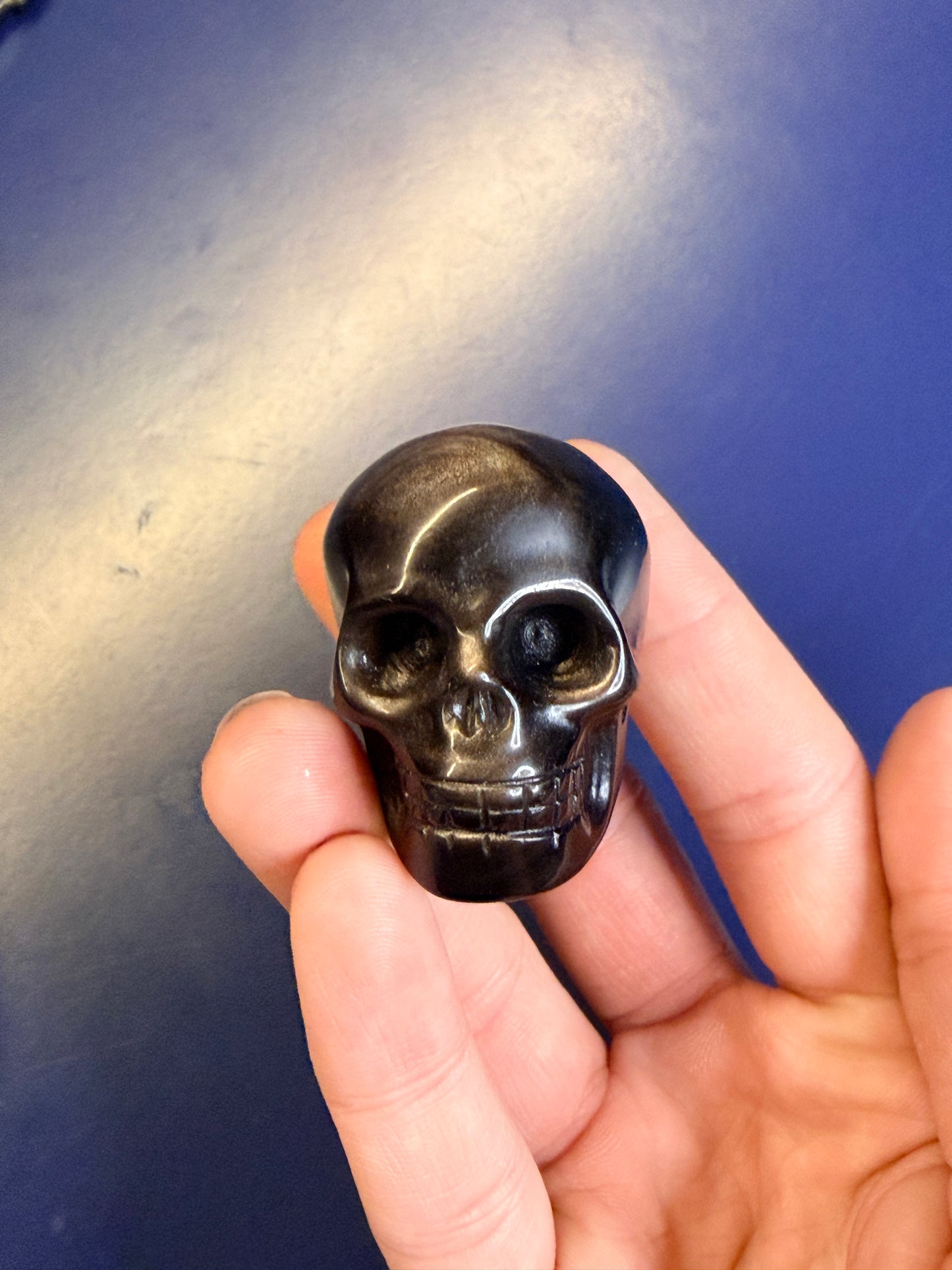 Hand holding a black and silver obsidian skull shape sitting against a blue background