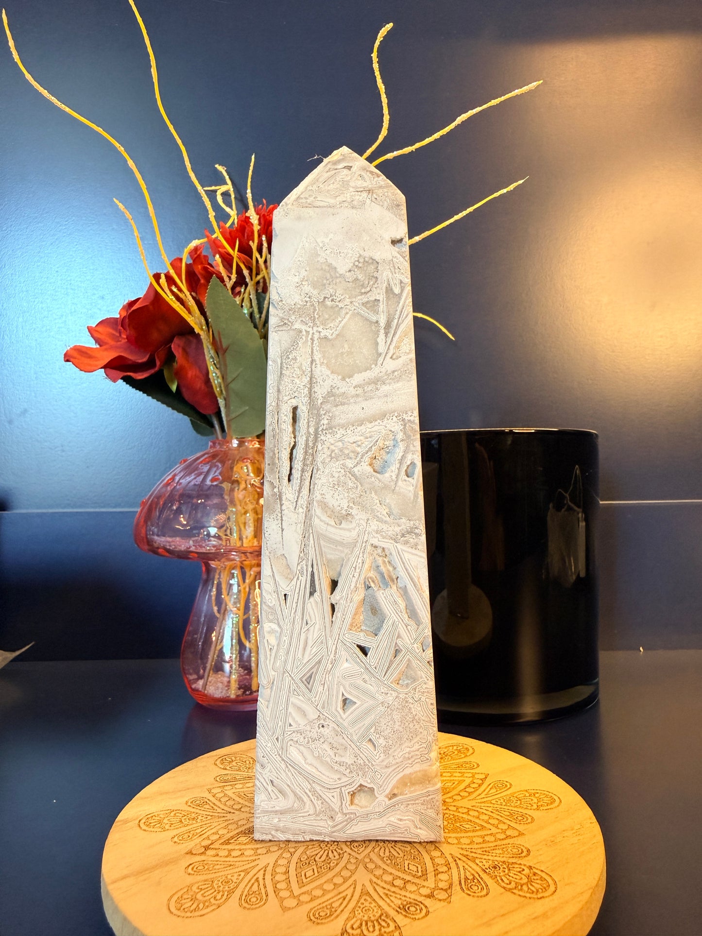 A large, intricate crystal tower sitting on a decorative wooden coaster in front of a glass mushroom and black jar