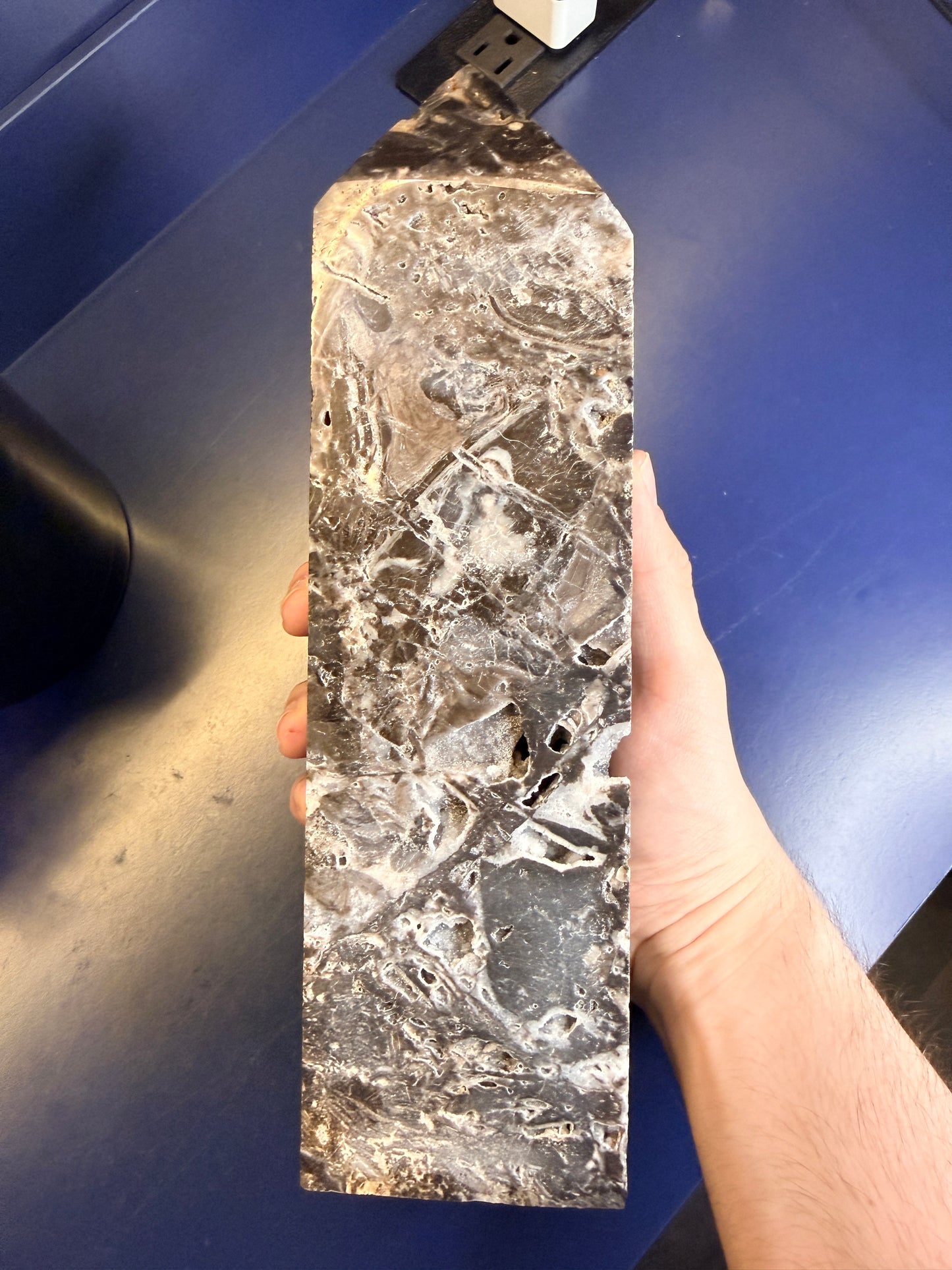 Hand holding a large grey and black sphalerite tower on a blue background