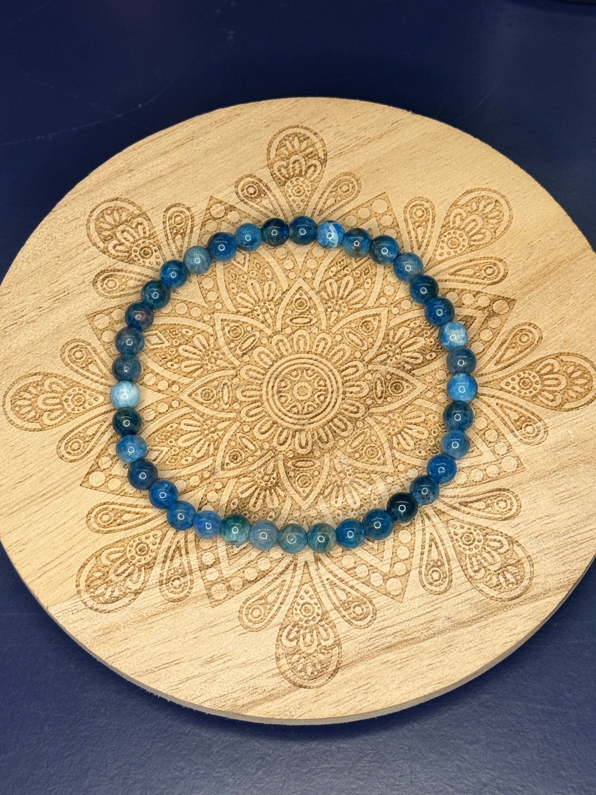 Blue beaded blue apatite bracelet on a decorative wooden coaster on a blue background