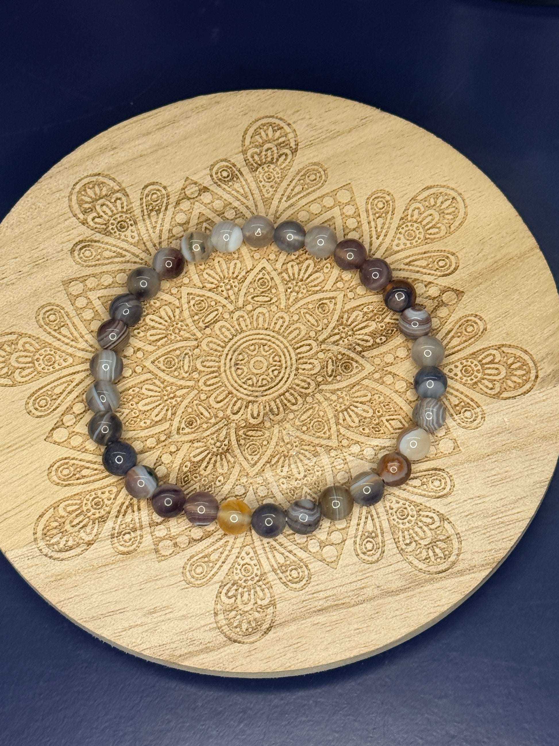 Multicolored beaded botswana agate bracelet resting on a decorative wooden coaster on a blue background