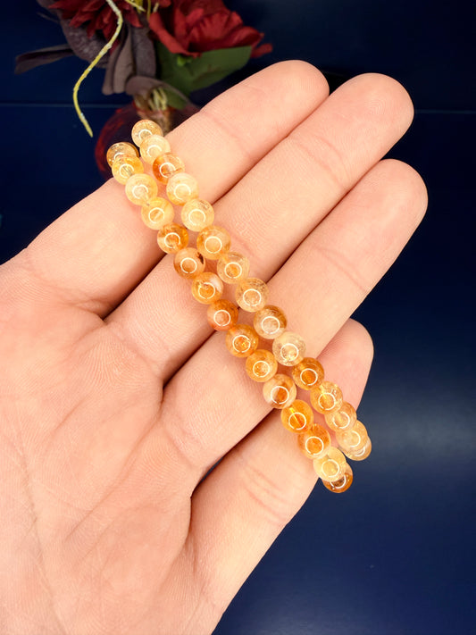 Hand holding two beaded yellow and orange citrine bracelets in front of a red flower on a blue background