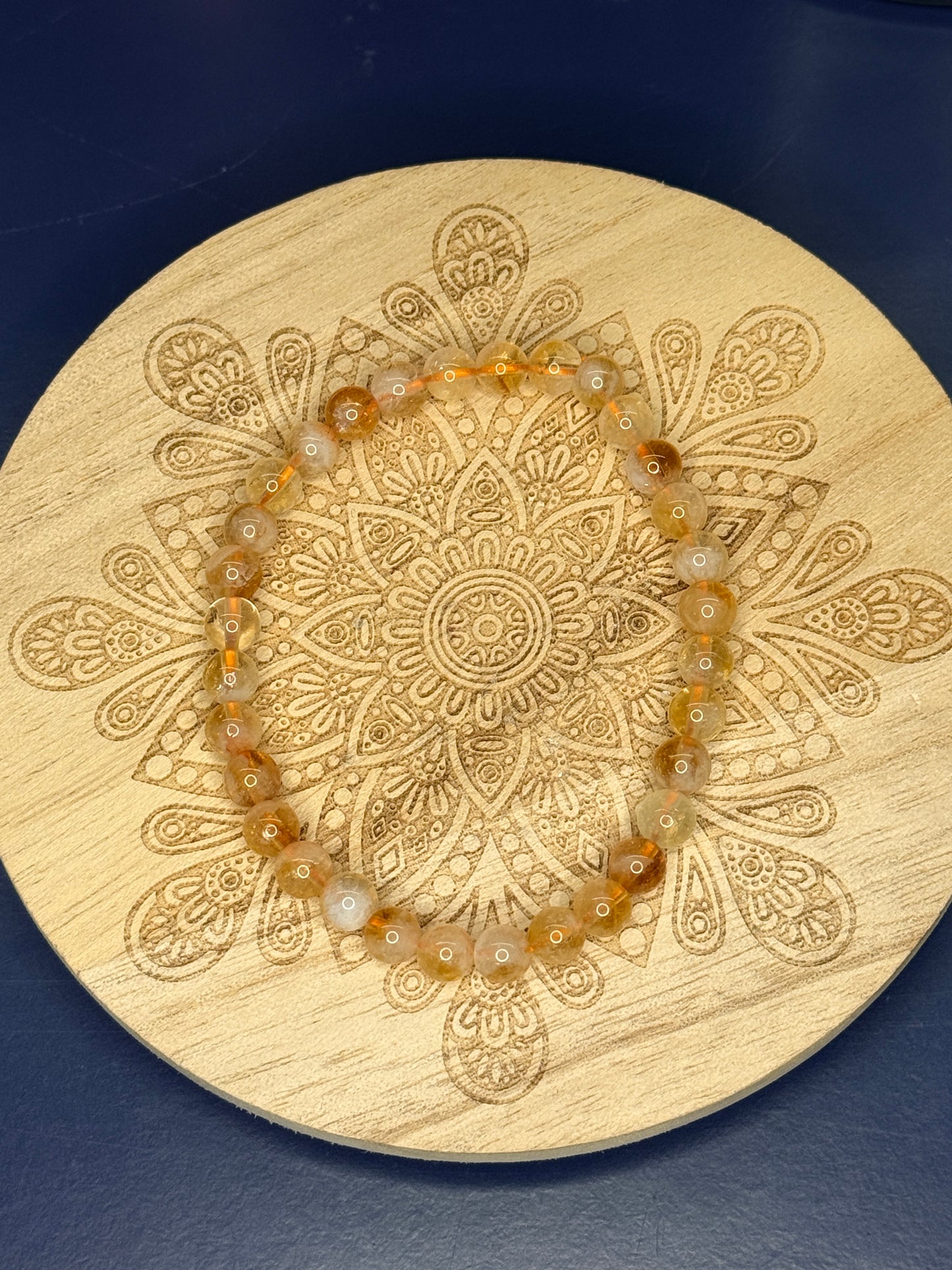 Yellow beaded citrine bracelet resting on a decorative wooden coaster on a blue background