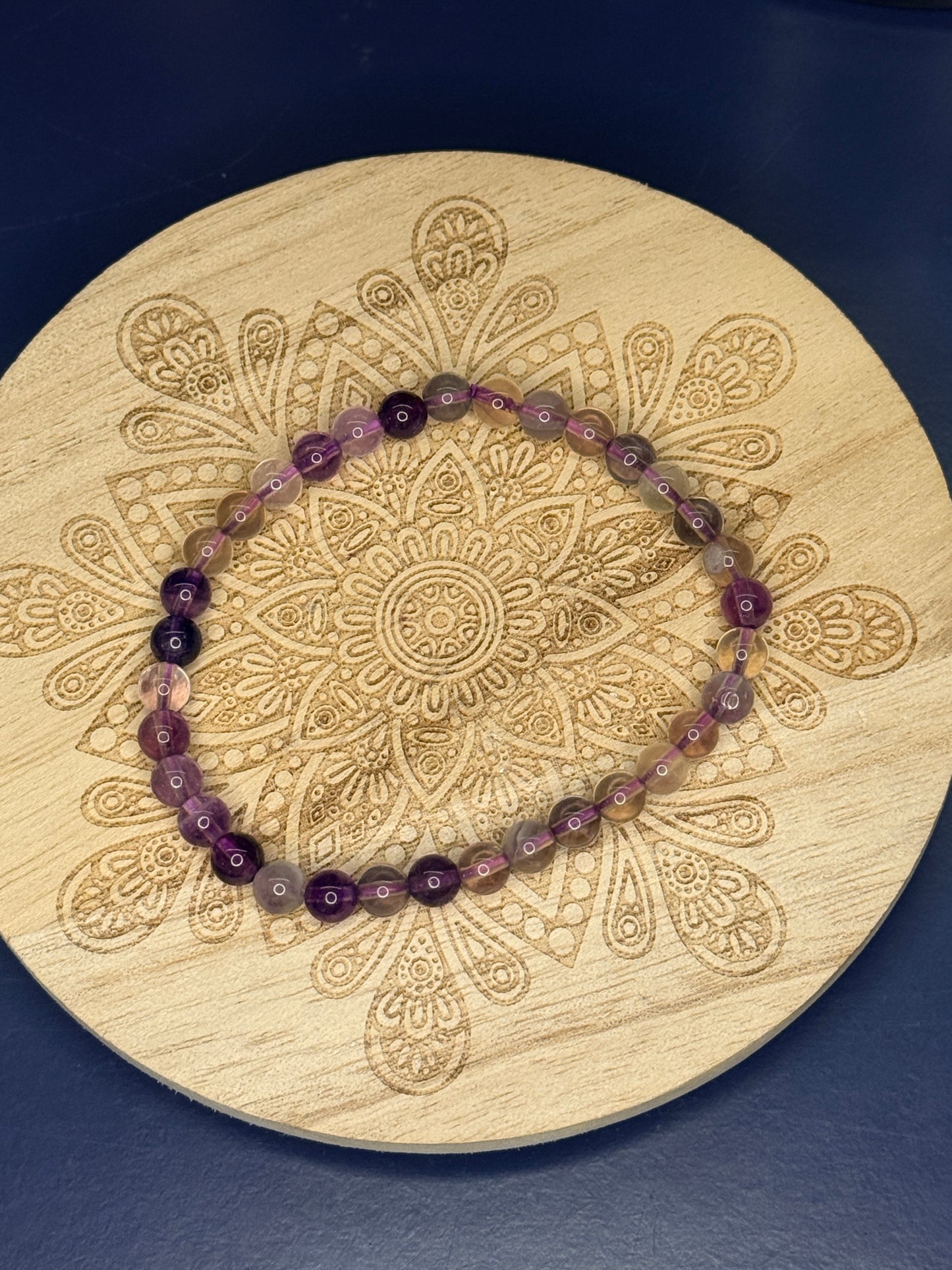 Translucent beaded fluorite bracelet resting on a decorative wooden coaster on a blue background