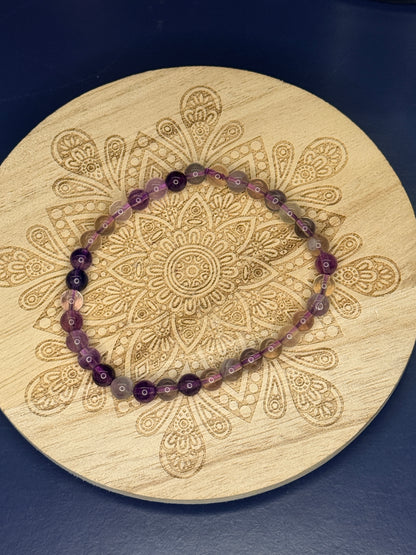 Translucent beaded fluorite bracelet resting on a decorative wooden coaster on a blue background