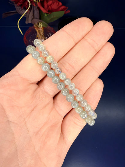 Hand holding two grey beaded labradorite bracelet in front of a red flower and blue background