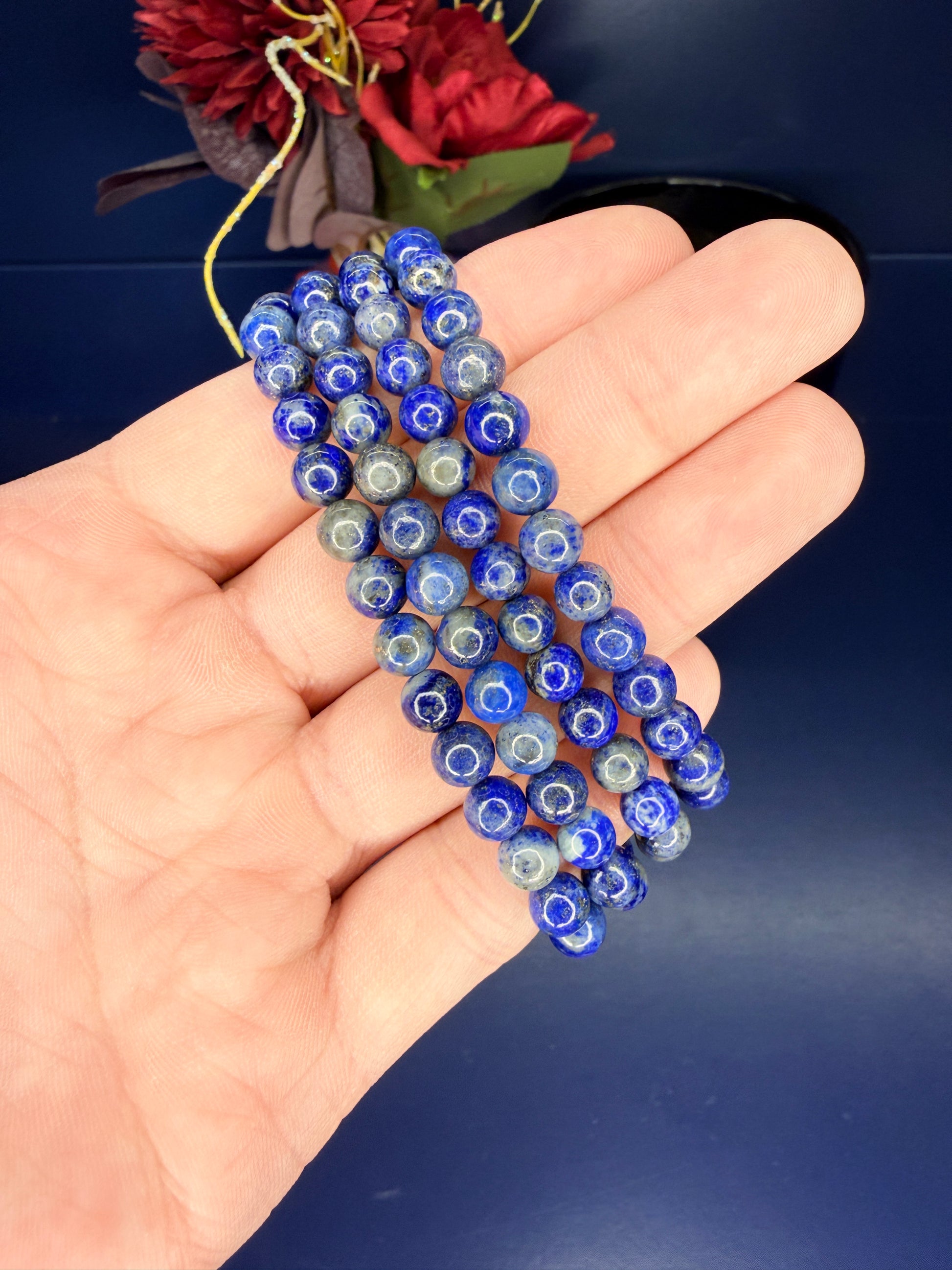 Hand holding four beaded lapis lazuli bracelets in front of red flowers on a blue background