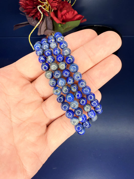Hand holding four beaded lapis lazuli bracelets in front of red flowers on a blue background