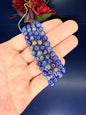 Hand holding four beaded lapis lazuli bracelets in front of red flowers on a blue background