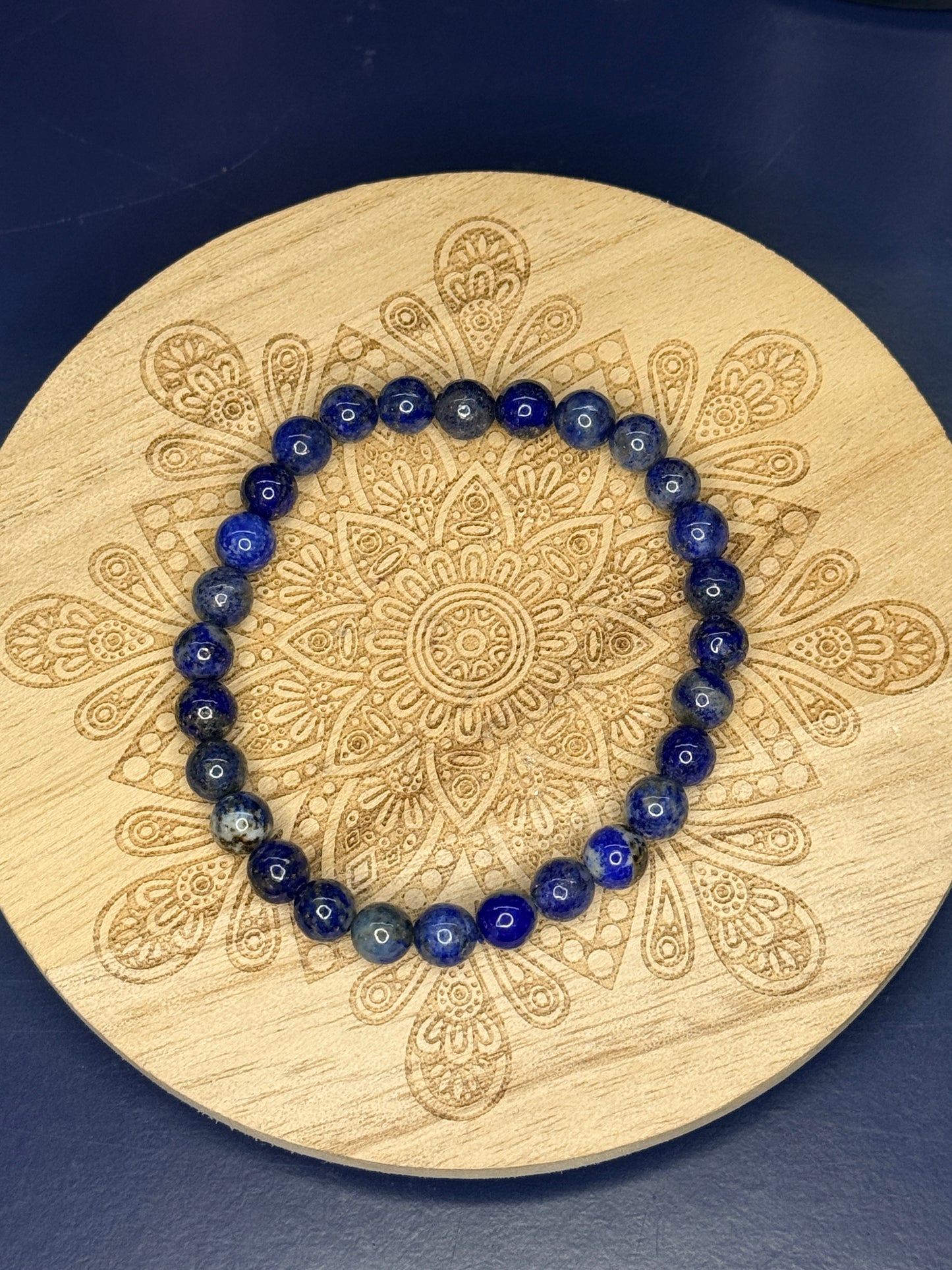 Blue beaded lapis lazuli bracelet resting on a decorative wooden coaster on a blue background
