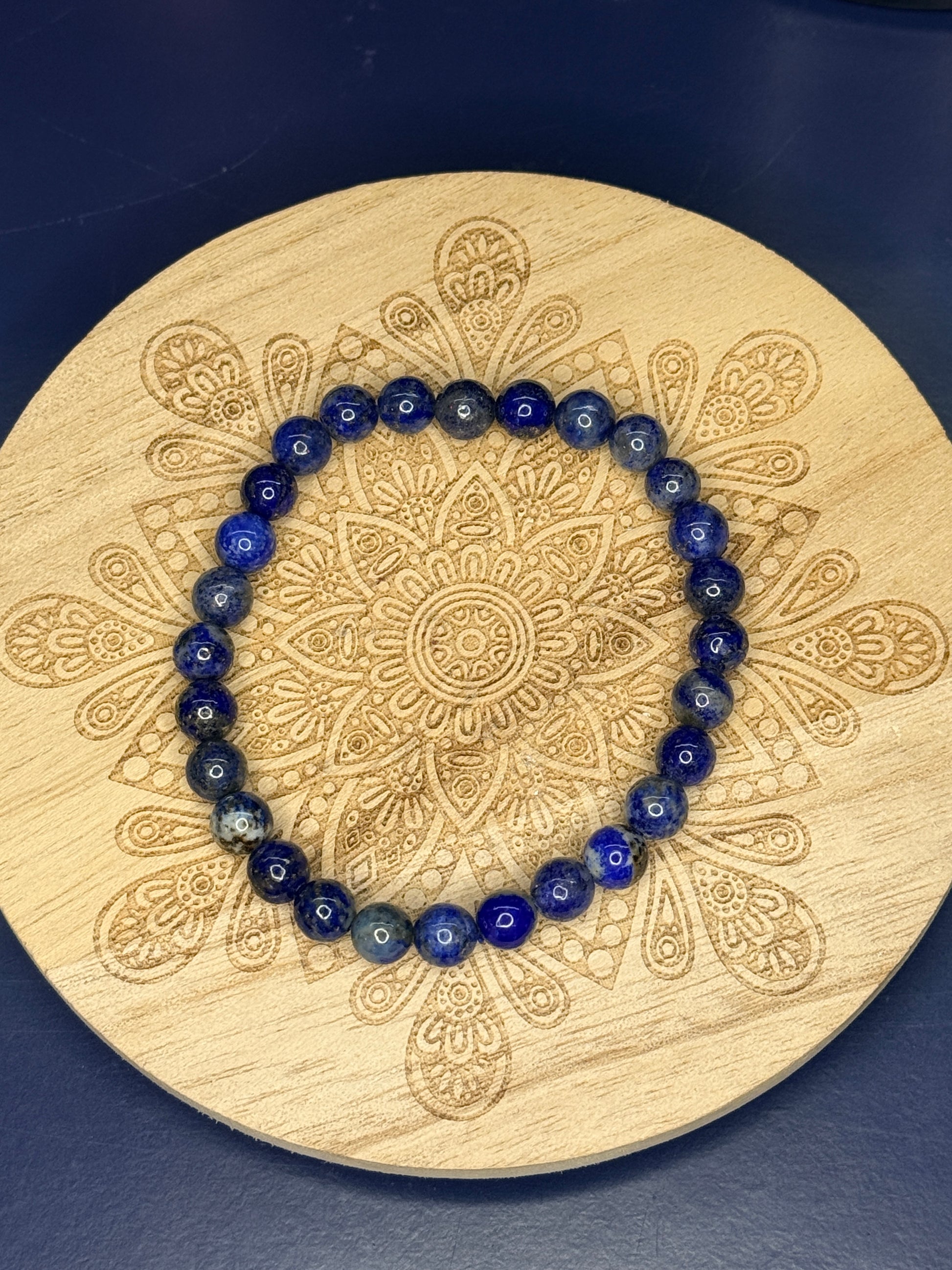 Blue beaded lapis lazuli bracelet resting on a decorative wooden coaster on a blue background