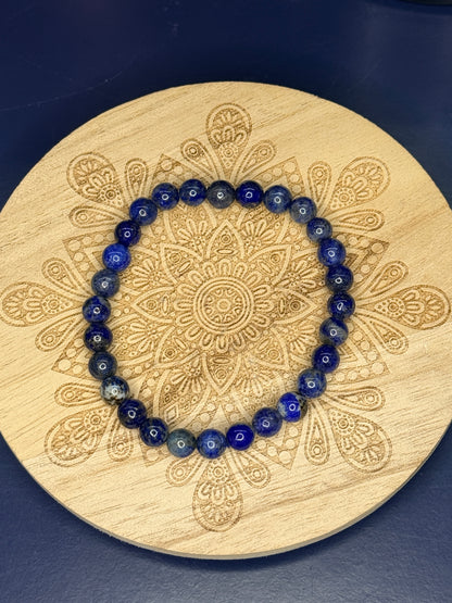 Blue beaded lapis lazuli bracelet resting on a decorative wooden coaster on a blue background