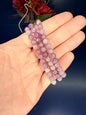 Hand holding three beaded purple lepidolite bracelets in front of a red flower on a blue background