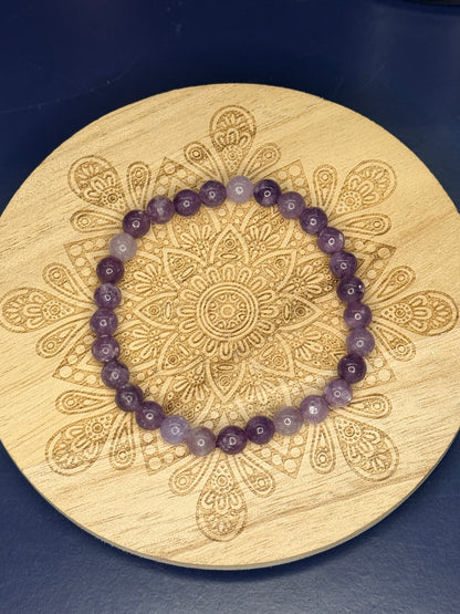 Purple beaded lepidolite bracelet resting on a decorative wooden coaster on a blue background