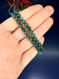 Hand holding two green beaded moss agate bracelets in front of a red flower on a blue background