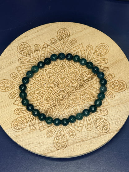 Green beaded moss agate bracelet resting on a decorative wooden coaster on a blue background