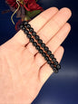 Hand holding two black beaded obsidian bracelets in front of a red flower on a blue background
