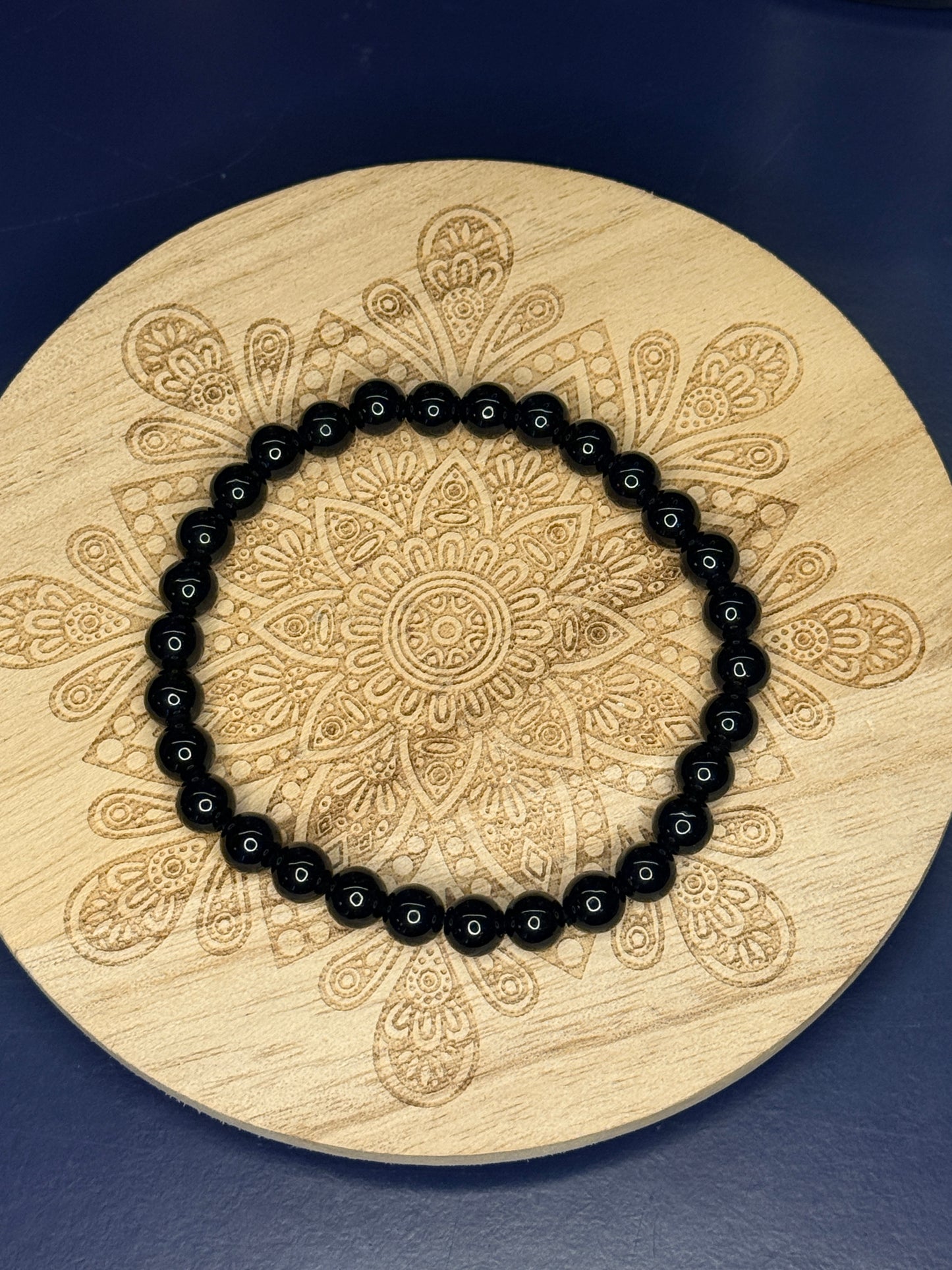 Black beaded obsidian bracelet resting on a decorative wooden coaster on a blue background