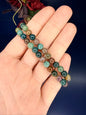 Hand holding two multicolored beaded ocean jasper bracelets in front of a red flower and blue background