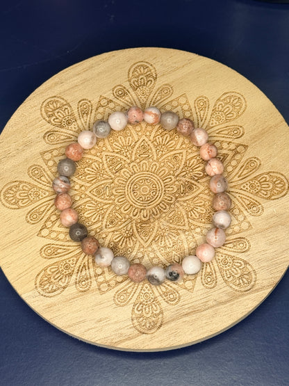 Beaded pink zebra jasper bracelet resting on a decorative wooden coaster on a blue background