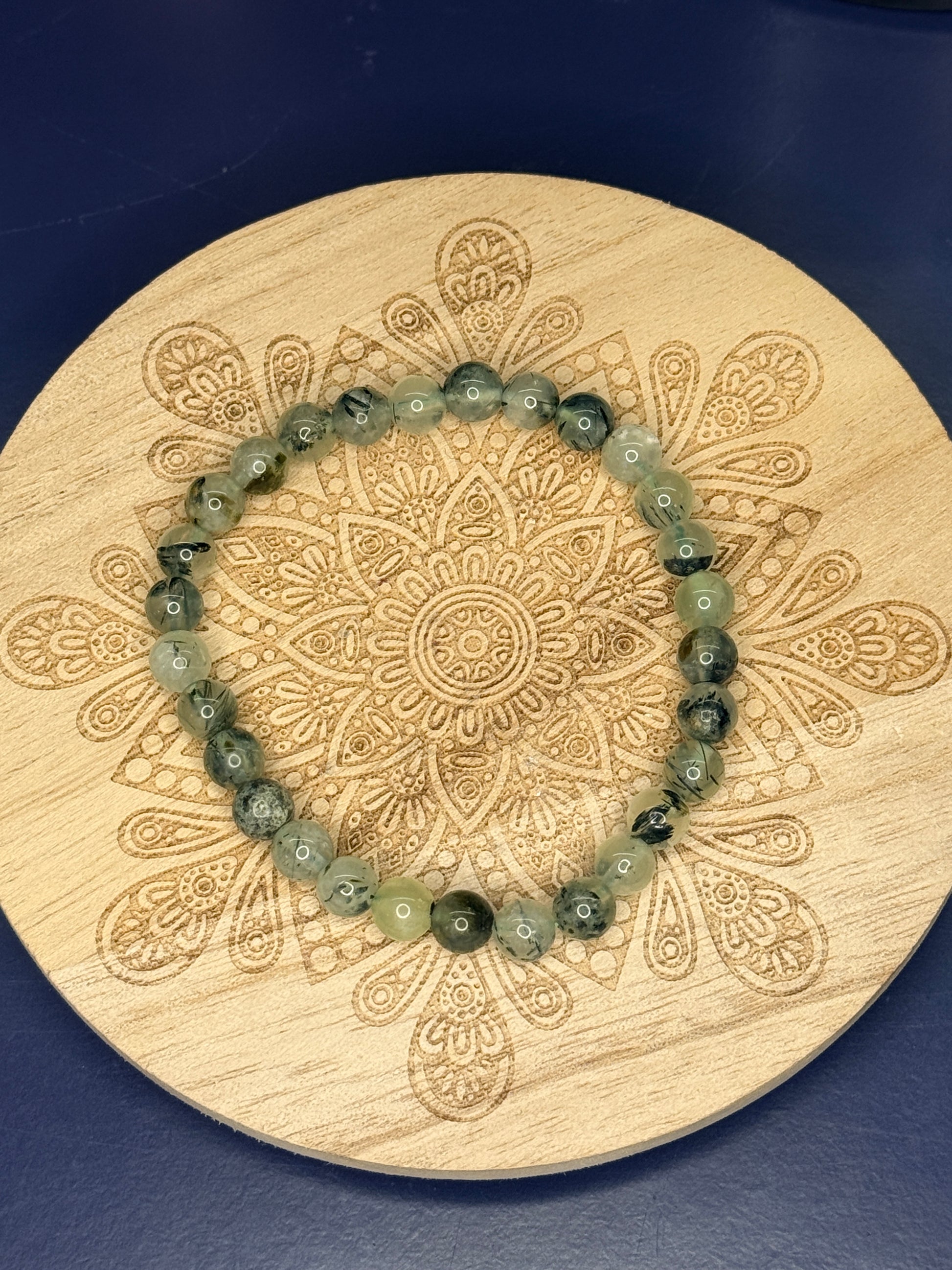 Beaded green prehnite bracelet resting on a decorative wooden coaster on a blue background