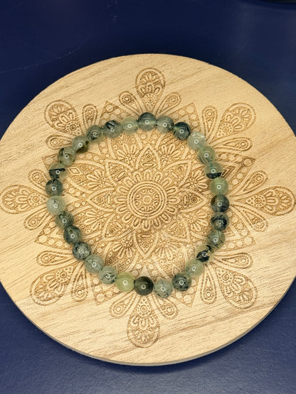 Beaded green prehnite bracelet resting on a decorative wooden coaster on a blue background