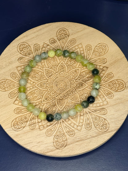 Green and yellow beaded serpentine bracelet resting on a decorative wooden coaster on a blue background