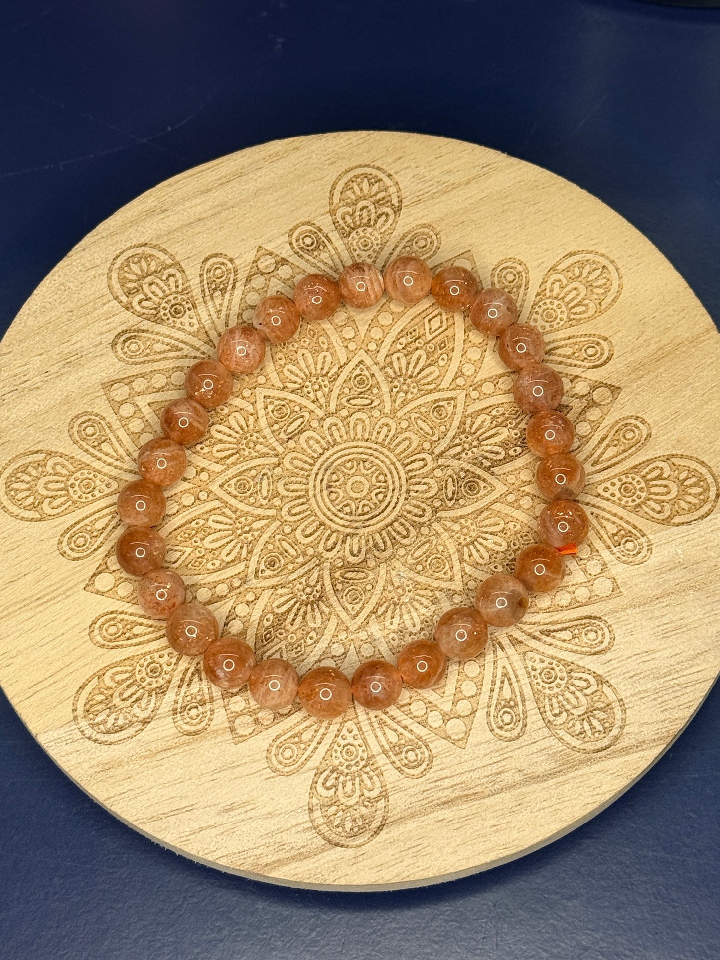 Orange beaded sunstone bracelet resting on a decorative wooden coaster on a blue background
