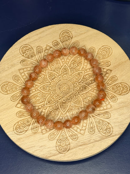 Orange beaded sunstone bracelet resting on a decorative wooden coaster on a blue background