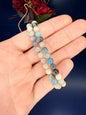 Hand holding two blue and beige beaded trolleite bracelets in front of a red flower and blue background