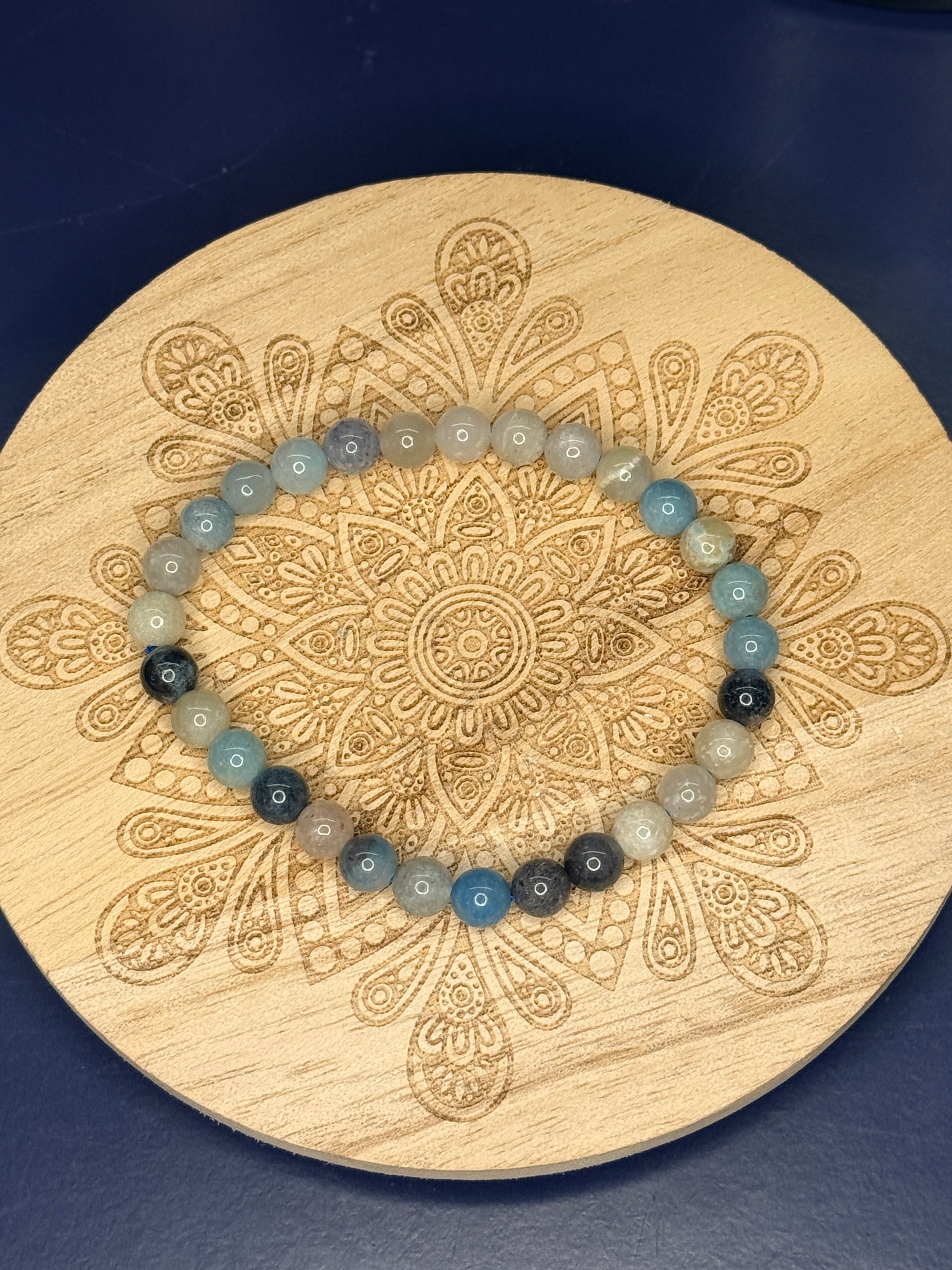 Blue and beige beaded trolleite bracelet resting on a decorative wooden coaster on a blue background