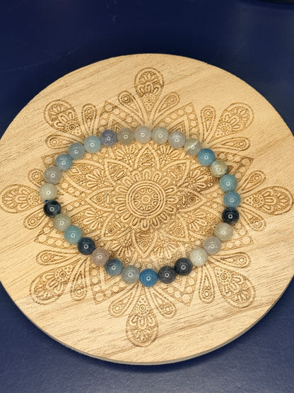 Blue and beige beaded trolleite bracelet resting on a decorative wooden coaster on a blue background