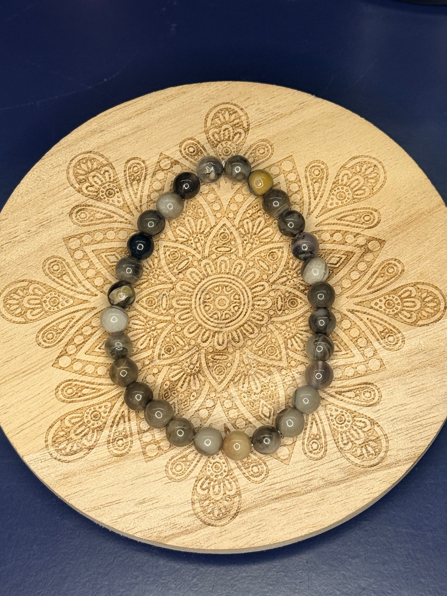 Multicolored beaded volcano agate bracelet resting on a decorative wooden coaster on a blue background