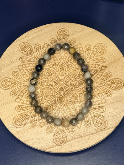 Multicolored beaded volcano agate bracelet resting on a decorative wooden coaster on a blue background