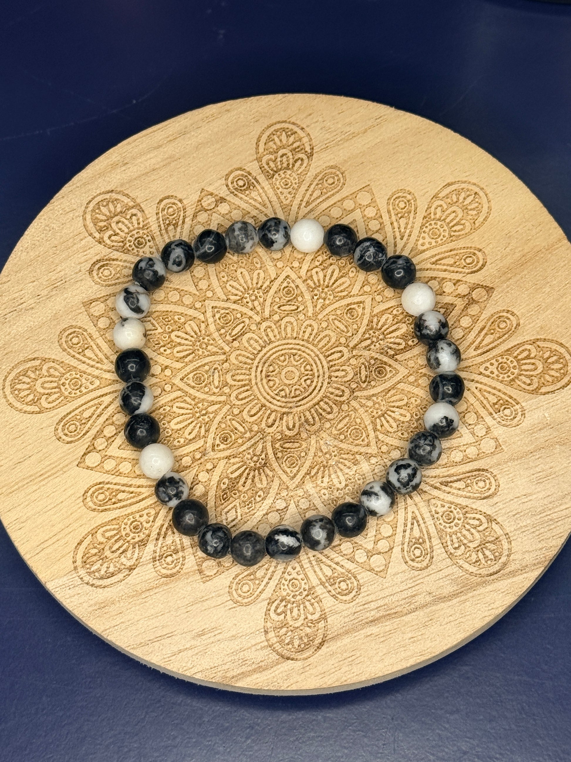 Black and white beaded zebra jasper bracelet resting on a decorative wooden coaster on a blue background